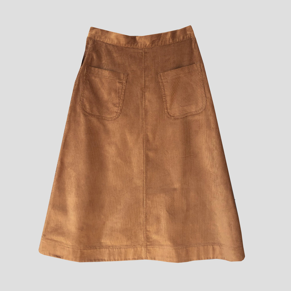 A brown corduroy A-line skirt with two back patch pockets, shown flat against a light gray background.