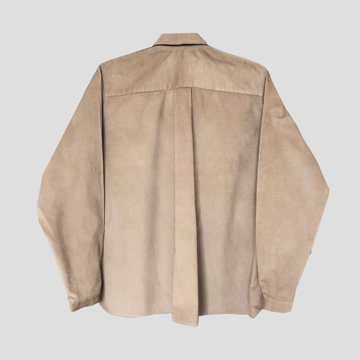 A light beige suede long-sleeve button-up shirt shown from the back, featuring a central vertical seam and stitched shoulder details, set against a solid light gray background.