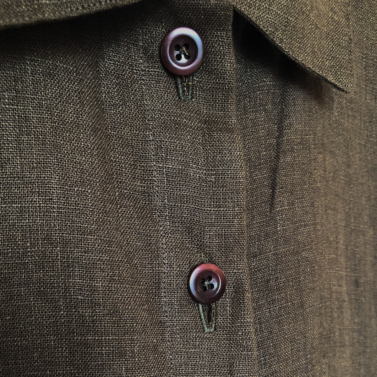 Close-up of a textured green linen dress with two dark brown buttons.